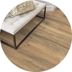 Close-up view of light oak-style laminate wood flooring next to a white tufted bench.