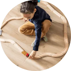 A child playing with a wooden toy train track set on light-colored luxury vinyl plank flooring.